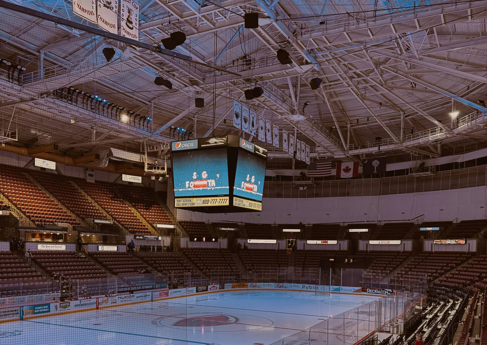 Empty hockey arena interior with overhead scoreboard, championship banners, and ice surface ready for a game.